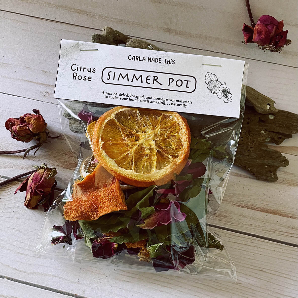 A bag of citrus rose simmer pot on a wooden table with dried roses behind it.