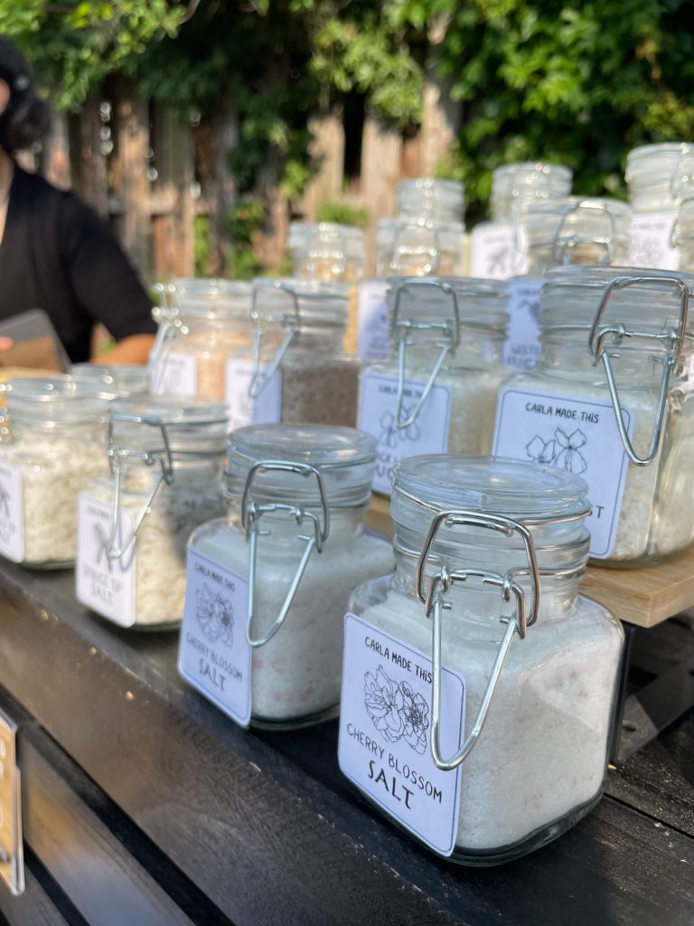 Many jars of salt lined up on a set of shelves at a popup sale.