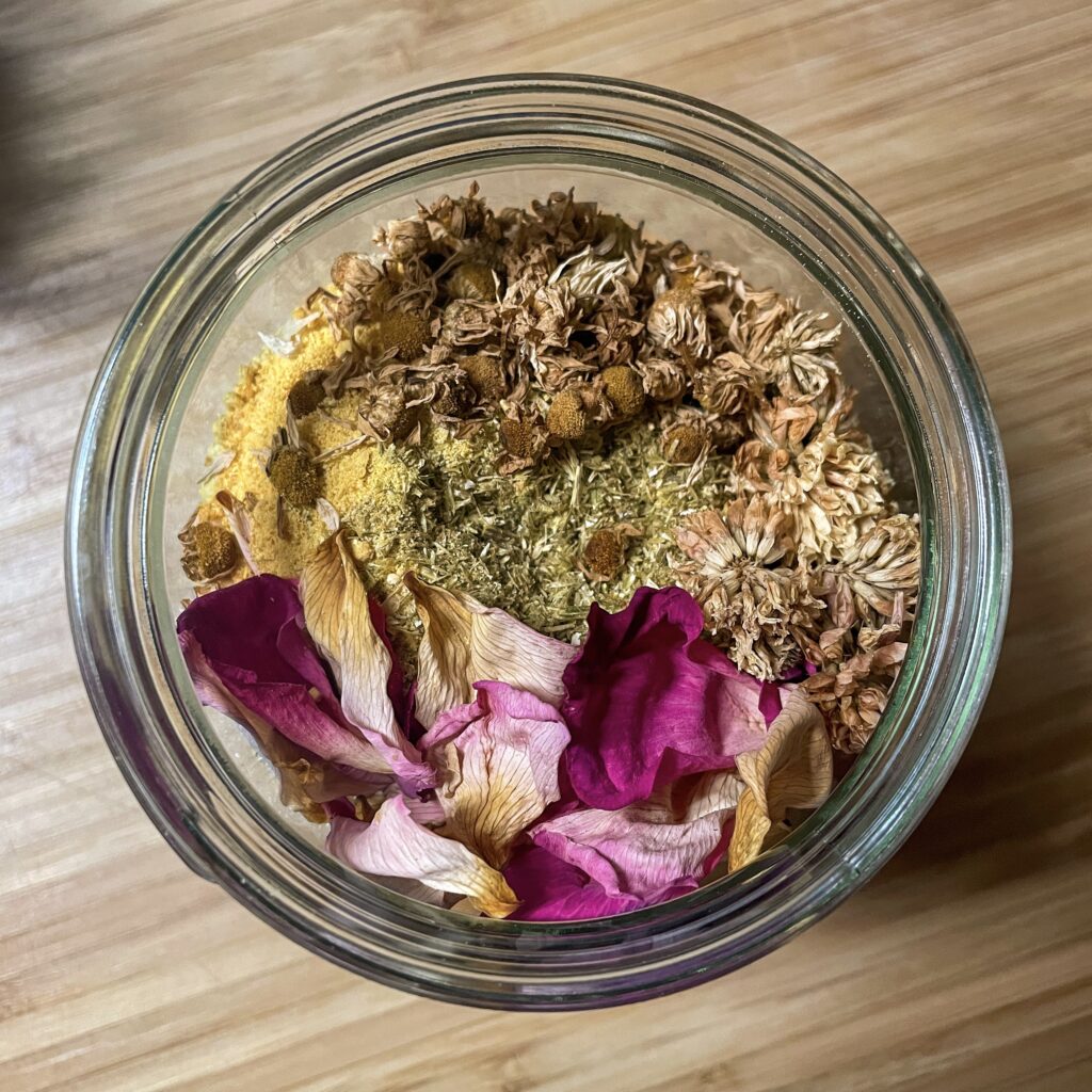 Dried herbs and flowers in a glass jar, looking from above.