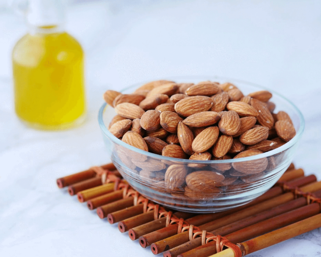 Bowl of raw almonds next to a bottle of sweet almond oil